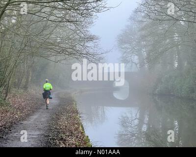 Adlington, Lancashire. Februar 2024. Wetter in Großbritannien: Nebel in Adlington, Lancashire. Ein nebeliger Morgen auf dem Leeds- und Liverpool-Kanal in Adlington. Läufer auf Schleppweg und Steinbrücke reflektiert in Canal Credit: Lancashire Images/StockimoNews/Alamy Live News Stockfoto