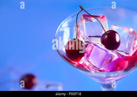 Cherry cocktail Close-up. Martini Glas mit Eiswürfeln und Kirschen auf einem blauen Hintergrund mit kopieren. Heißer Sommertag Erfrischung Konzept Stockfoto