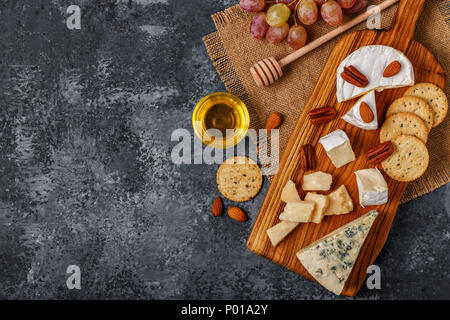 Sortiment von Käse mit Honig, Nüsse und Trauben auf einem Schneidebrett, Ansicht von oben. Stockfoto