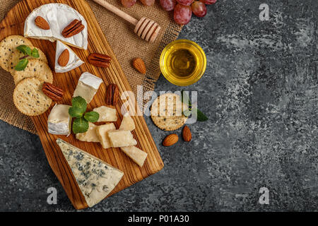 Sortiment von Käse mit Honig, Nüsse und Trauben auf einem Schneidebrett, Ansicht von oben. Stockfoto