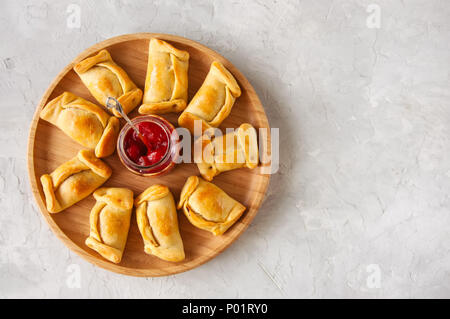 Blick von oben auf die chilenischen Empanadas auf einer Holzplatte mit Ketchup. Weißer Stein Hintergrund. Stockfoto