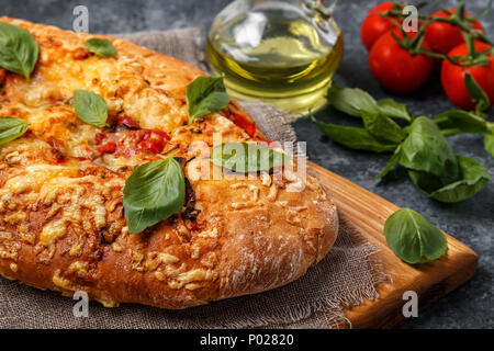 Focaccia mit Tomaten, Kräutern und Käse, garniert mit Basilikum. Stockfoto