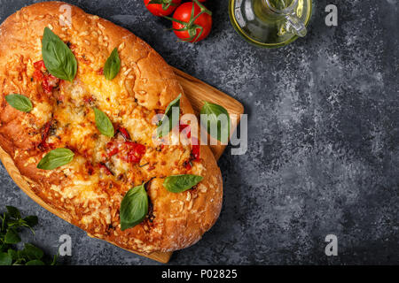 Focaccia mit Tomaten, Kräutern und Käse, garniert mit Basilikum. Stockfoto