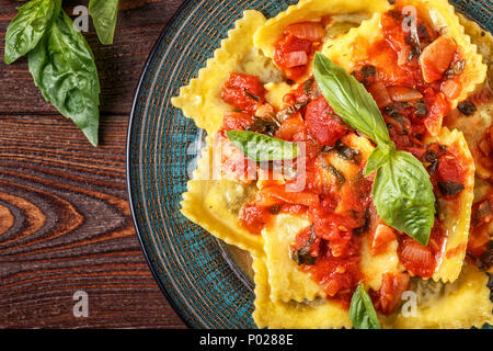 Ravioli mit Tomatensauce und Basilikum auf dunklem Hintergrund, Ansicht von oben. Stockfoto