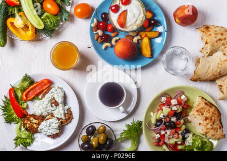 Griechische Vorspeisen - Krapfen von Zucchini mit Tzatziki Sauce, Griechischer Salat, Joghurt mit frischem Obst und Nüsse, Oliven, Gemüse und Kräuter, Ansicht von oben. Stockfoto