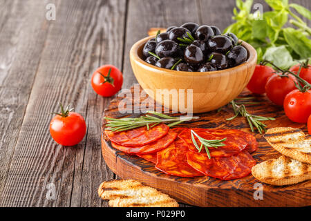 Spanische traditionelle Chorizo Wurst mit frischen Kräutern, Oliven, Tomaten auf einem Holzbrett. Stockfoto