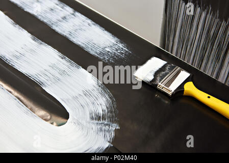 Pinsel und weiße Farbe auf eine schwarze Fläche Stockfoto