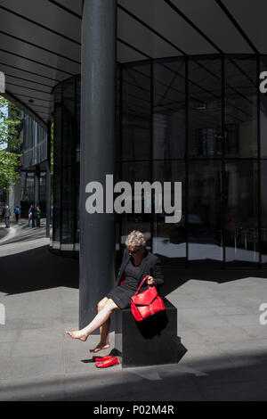 Eine Frau ruht Ihre Füße in einem kleinen Bereich des Sonnenlichts auf Fenchurch Avenue in der Innenstadt von London - Financial District in der Hauptstadt, am 6. Juni 2018 in London, England. Stockfoto