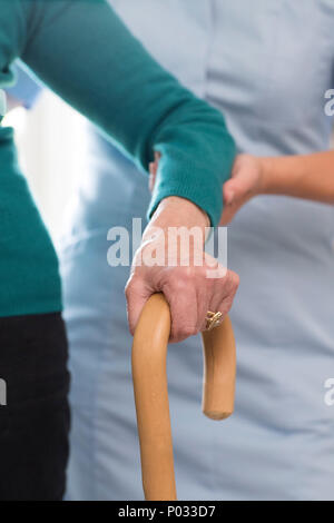 Senior womans Hände auf Gehstock mit Sorgfalt Arbeiter im Hintergrund Stockfoto