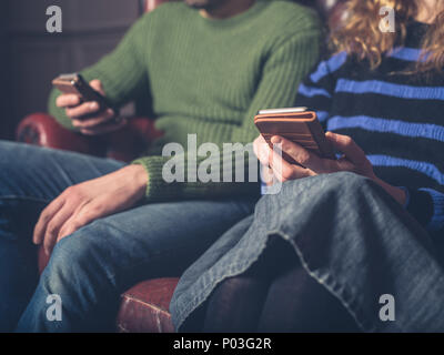 Ein Mann und eine Frau sitzen auf einem Sofa mit Ihren smart phones Stockfoto