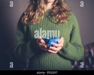 Eine junge Frau das Tragen einer Brücke befindet sich in einem Wohnzimmer, mit einer Tasse Kaffee Stockfoto