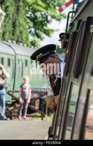 Vorderansicht der Zugbegleiter (Guard) in Uniform, auf vintage UK Dampfzug, Kopf aus Fenster als Zug geht Heritage Railway Station. Stockfoto