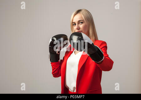 Junge schöne weiße blonde Frauen in einem hellen Rot strengen Anzug mit einer Jacke und weisse Bluse in einer Pose mit Boxhandschuhen auf einem weißen isoliert Stockfoto