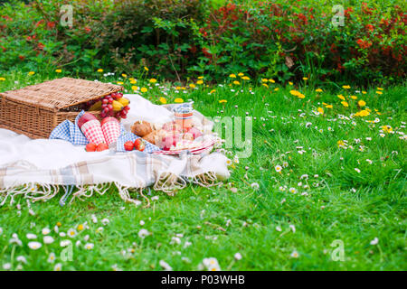 Picknickkorb. Essen auf grünem Gras und Plaid. Feder und Ferienhäuser. Für Text platzieren. Stockfoto