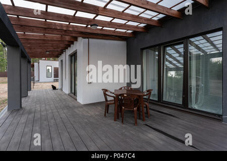 Seitenansicht eines offenen Veranda vor einem modernen Forest Cottage. Kiefer junge Wald unter den Sonnenuntergang strahlen im Hintergrund. Stockfoto