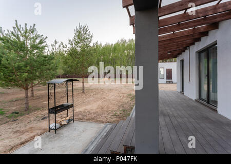 Seitenansicht eines offenen Veranda vor einem modernen Forest Cottage. Kiefer junge Wald unter den Sonnenuntergang strahlen im Hintergrund. Stockfoto