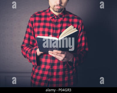 Ein junger Mann mit einem roten Flanellhemd ist das Lesen eines Buches in ein luxuriöses Wohnzimmer Stockfoto