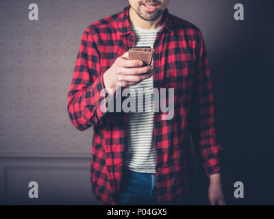 Ein junger Mann mit einem roten Flanellhemd ist zu Hause in ein luxuriöses Wohnzimmer mit seinem Smart Phone Stockfoto