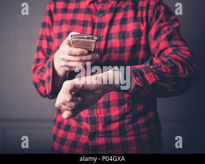 Ein junger Mann mit einem roten Flanellhemd ist zu Hause in ein luxuriöses Wohnzimmer mit seinem Smart Phone und beobachten Stockfoto