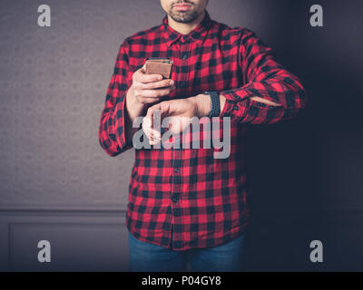 Ein junger Mann mit einem roten Flanellhemd ist zu Hause in ein luxuriöses Wohnzimmer mit seinem Smart Phone und beobachten Stockfoto