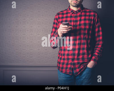 Ein junger Mann mit einem roten Flanellhemd ist zu Hause in ein luxuriöses Wohnzimmer mit seinem Smart Phone Stockfoto