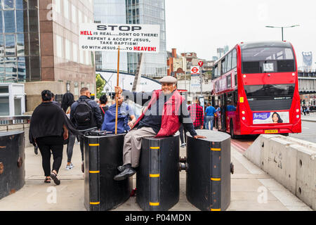 Mann mittleren Alters, der religiösen Spoiler mit einem Plakat, sitzt auf den Anti-terror-Fahrzeug Barrieren auf die London Bridge durch Borough Market, London SE1 Stockfoto