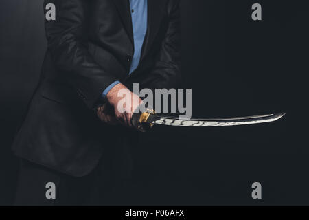 7/8 Schuß von Mann in Anzug Holding japanische Katana Schwert auf Schwarz Stockfoto