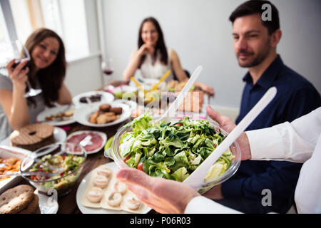 Nahaufnahme von einem Kellner bringen neue Schale mit frischem Salat auf den Tisch Stockfoto