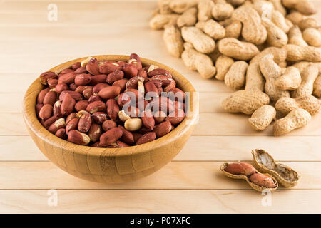 Hölzerne Schüssel voller geschälte Erdnüsse und Erdnüsse in Kürze auf einem Holztisch Stockfoto