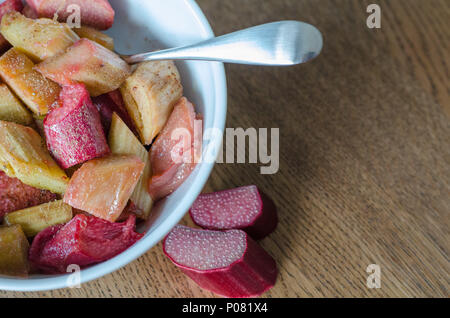 Weiße Schüssel mit Rhabarberkompott und kleine Löffel auf Holz- Hintergrund. close-up. Stockfoto