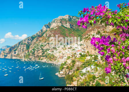 Defokussierten Blick auf kleine Küstenstadt auf der Bergseite mit lila Blüten im Vordergrund an sonnigen Sommertagen, Positano, Amalfi, Kampanien, Italien Stockfoto