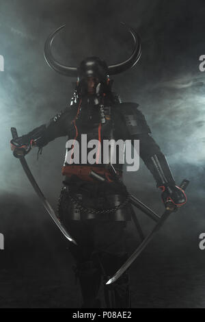 Samurai in traditioneller Rüstung mit zwei Katana Schwerter auf dunklem Hintergrund mit Rauch Stockfoto