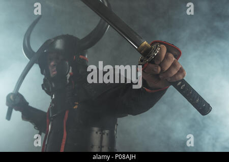 Nahaufnahme der Samurai in Rüstung mit zwei Katana Schwerter auf dunklem Hintergrund mit Rauch Stockfoto