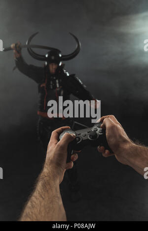 7/8 Schuß von Mann controlling Samurai Charakter mit Gamepad auf Schwarz Stockfoto