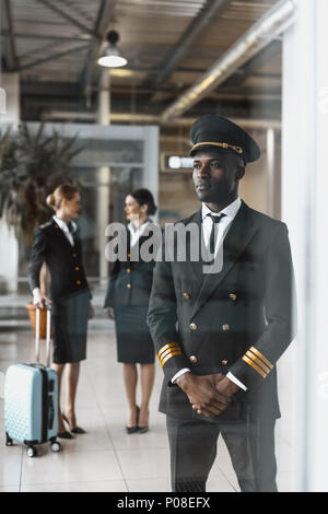 Hübscher junger Pilot im Flughafen mit stewardessen vor dem Flug Stockfoto