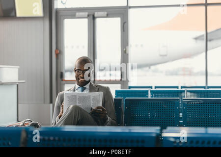 Gut aussehender Geschäftsmann lesen Zeitung beim Warten auf der Reise am Flughafen Lobby Stockfoto
