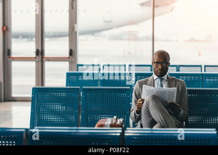 Ernsthafte Geschäftsmann lesen Zeitung warten auf der Reise am Flughafen Lobby Stockfoto