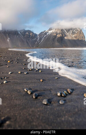 Steine am schwarzen Sandstrand, Berge, und Eystrahorn Klifatindur Kambhorn, landspitze Stokksnes, Gebirge Klifatindur Stockfoto