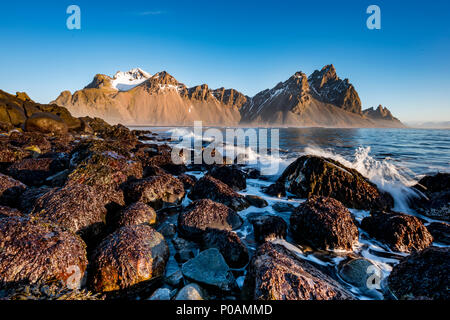 Wellen schlugen an der Küste, in den Bergen, und Eystrahorn Klifatindur Kambhorn, landspitze Stokksnes, Gebirge Klifatindur Stockfoto