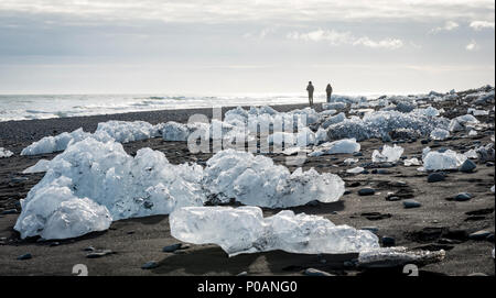 Zwei Touristen zu Fuß am Strand, Eisschollen auf schwarzem Lavasand, Diamond Beach, Fjallsárlón Gletscherlagune, East Iceland Stockfoto