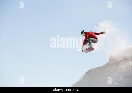 Bild des Menschen in der Helm mit Snowboard springen von Verschneiten Berghang Stockfoto