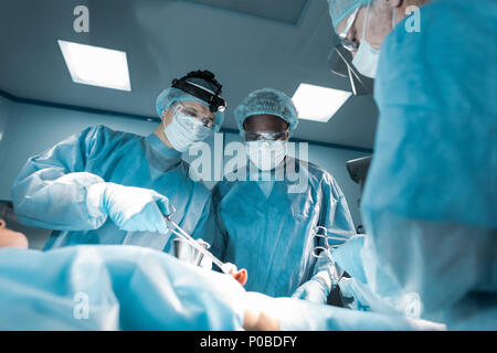 Ansicht von unten auf das multikulturelle Chirurgen und Patienten im OP Stockfoto