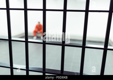 Gefangener sitzt auf der Bank mit Gefängnis Bars im Vordergrund Stockfoto