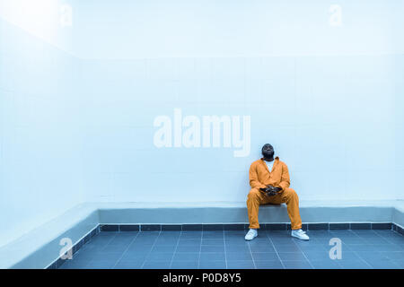 African American Gefangener sitzt auf der Bank in der Gefängniszelle Stockfoto