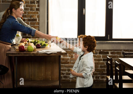 Seitenansicht der lächelnde Frau Apple, Sohn beim Kochen Abendessen mit Mann zu Hause Stockfoto