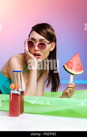 Frau in Sonnenbrille holding Wassermelone Stück beim Entspannen auf Schwimmen Matratze Stockfoto