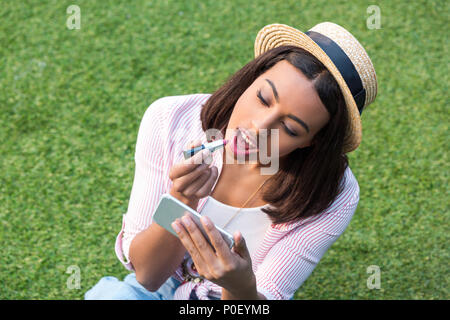 Schönen lächeln African American Girl Anwendung Make-up Während der Sitzung auf grünem Gras Stockfoto