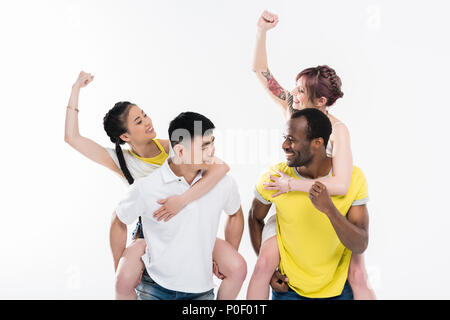 Jungen multiethnischen Männer huckepack schönen lächelnden Mädchen isoliert auf weißem Stockfoto