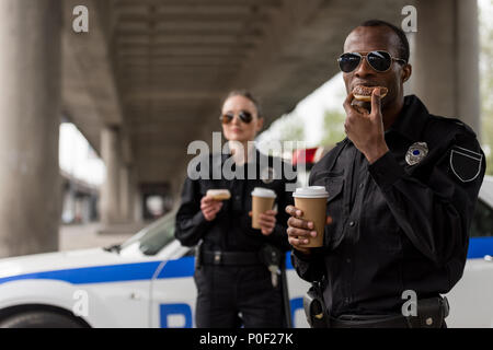 Jungen Polizisten in Kaffeepause mit Donuts vor der Polizei Auto Stockfoto