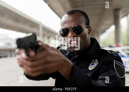 Wütend afrikanische amerikanische Polizisten schreien und die darauf abzielt, durch die Pistole Stockfoto